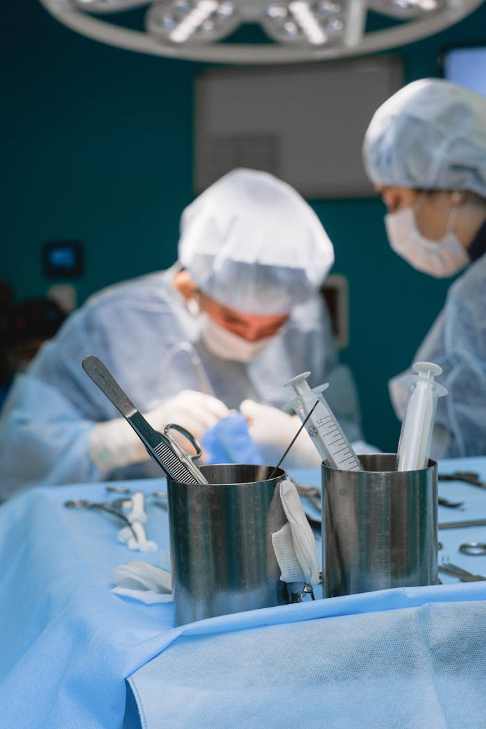 Two surgeons in blue scrubs performing surgery in a hospital operating room, focused on surgical precision.